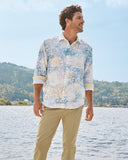 Man wearing a floral shirt by a lake with mountains in the background