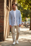 Man wearing a light blue  and white blazer over a white shirt and beige pants, standing on a sidewalk.