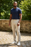 Man wearing a navy shirt and beige pants standing outdoors with greenery in the background