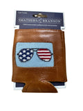 A brown leather can cooler wallet by Smathers & Branson, featuring a cross-stitched American flag design on the front. The item is shown in its retail packaging on a light wood background.
