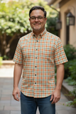 Man wearing a plaid shirt standing outdoors with greenery in the background