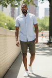 Man wearing a light blue shirt, green shorts, and white sneakers walking outdoors.