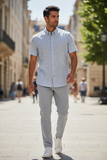 Man walking on a street wearing a light blue patterned shirt and gray pants.