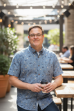 Man holding a coffee cup in an outdoor setting with tables and plants.