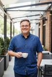 Man in a blue plaid shirt holding a cup outdoors
