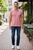 Man wearing a rose polo shirt and blue jeans standing on a sidewalk.