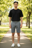 Man wearing a black t-shirt and gray shorts standing on a path in a park.