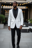 Man wearing a white tuxedo with black lapels and pants in an outdoor setting.