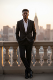 Man in a black suit standing on a balcony with a city skyline in the background