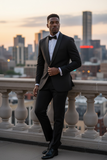 Man in a black suit standing on a balcony with a city skyline in the background