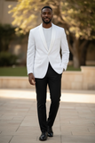 Man wearing a white blazer and black pants standing outdoors.