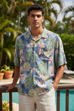 Man wearing a tropical leaf patterned shirt standing by a pool with greenery in the background