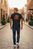 Man walking down a street wearing a black t-shirt with graphic design on the back.
