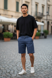 Man wearing a black t-shirt and blue shorts standing on a cobblestone street.