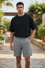 Man wearing a black t-shirt and gray shorts standing outdoors with plants in the background