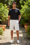 Man wearing a black t-shirt and white shorts standing in a garden with potted plants.