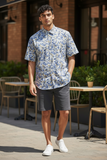 Man wearing a blue floral shirt and dark shorts standing outdoors.