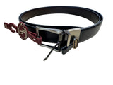A black leather belt with a silver-toned metal buckle and a red hangtag, displayed on a light wood tabletop.