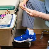 Person in scrubs with a blue shoe stepping onto a scale in a medical setting.