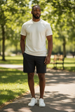Man standing on a path in a park wearing a white t-shirt and dark shorts.