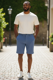 Man wearing a white t-shirt and blue shorts standing on a cobblestone street.