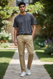Man wearing a gray t-shirt and beige pants standing on a stone path with greenery in the background