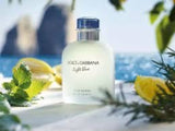 Dolce & Gabbana light blue perfume bottle with lemons and mint leaves on a beach.