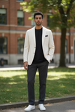 Man wearing a beige blazer, black shirt, and gray pants standing outdoors.