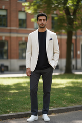 Man wearing a beige blazer, black shirt, and gray pants standing outdoors.