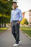 Man in a light blue shirt and midnight pants walking on a path with trees and buildings in the background